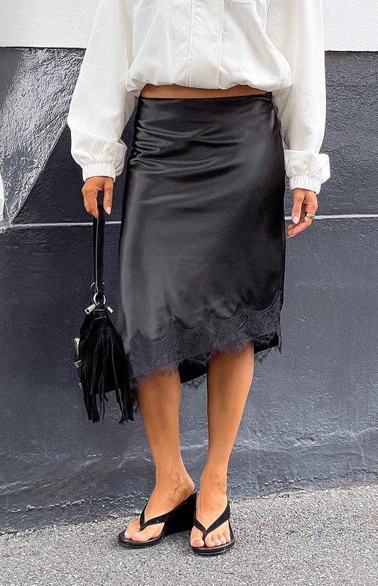 Front view of a black satin midi skirt with a scalloped lace trim hem and a flowing silhouette