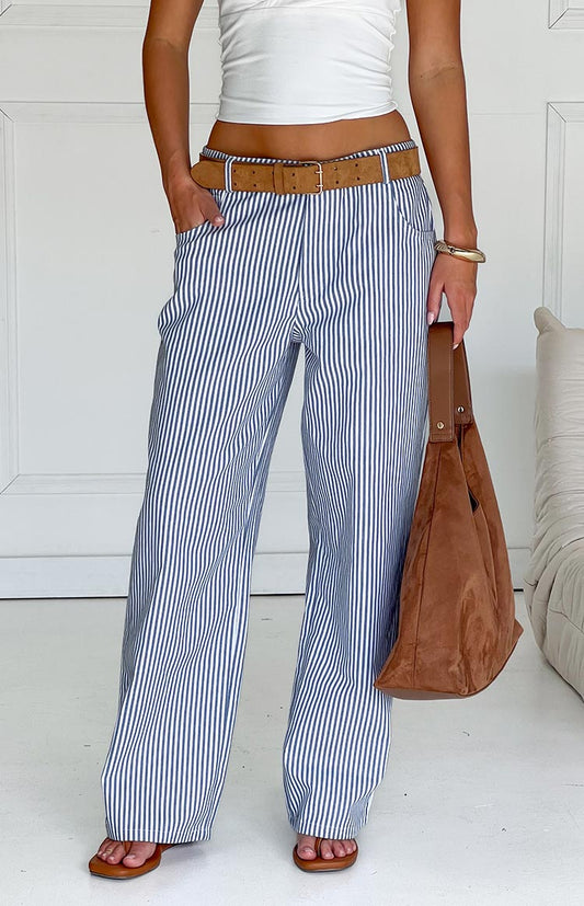 Model wears blue and white striped pants with a white top, brown belt, and matching handbag, showcasing stylish wide-leg trousers.