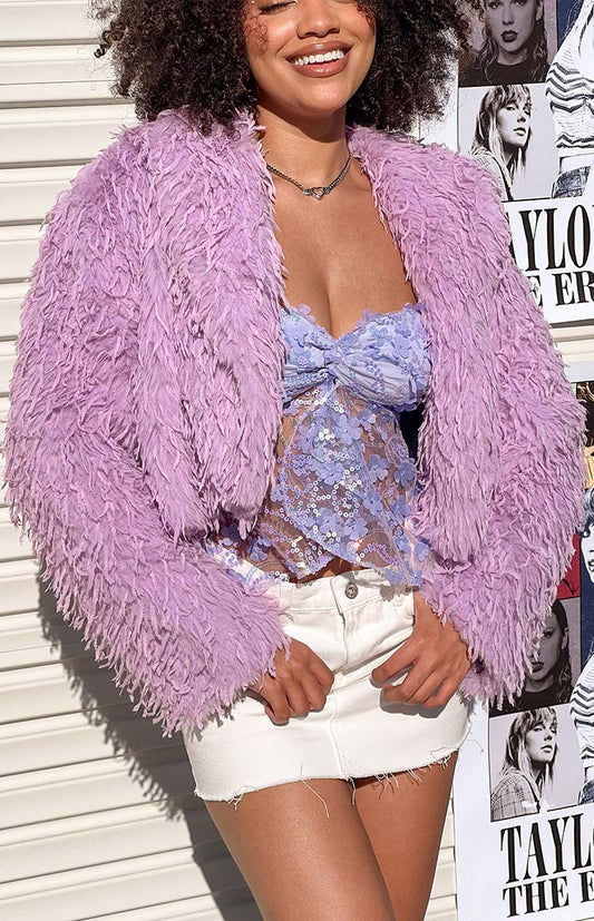 Girl standing in front of a wall wearing a purple fringe jacket over a purple top and white skirt. 