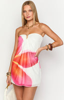 Blonde model wearing a white strapless mini dress with an oversized frangipani placement print and gold U bar detail at the bust