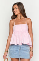 Model with light pink gingham halter top standing in front of a plan and a house with a brown bag in hand.