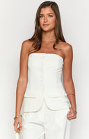 Model wearing white strapless top and white pants holding orange cocktail glass.