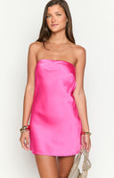 Girl showing the back of a hot pink satin mini dress. The formal dress features a stylish open cowl back that fastens with a delicate tie, making it a standout choice for homecoming.