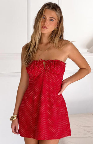 Fashion model showcasing a playful red and white polka dot strapless mini dress with a ruffled neckline and charming front tie, perfect for a casual or festive occasion.