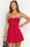 Fashion model showcasing a playful red and white polka dot strapless mini dress with a ruffled neckline and charming front tie, perfect for a casual or festive occasion.