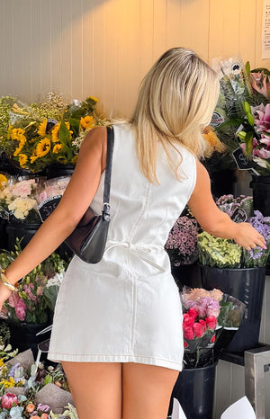 Back view of a crisp white wash denim mini dress, featuring a sleeveless design and a unique self-tie detail at the waist, offering a casual yet stylish silhouette.