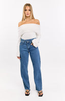  A woman crouches to show the back detail of her mid-wash jeans, which feature a white scalloped embroidered trim along the top of the back pockets. She is wearing a blue and white gingham top and yellow sneakers.