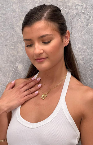 girl is wearing a gold bow knot pendant necklace with a white halter top 