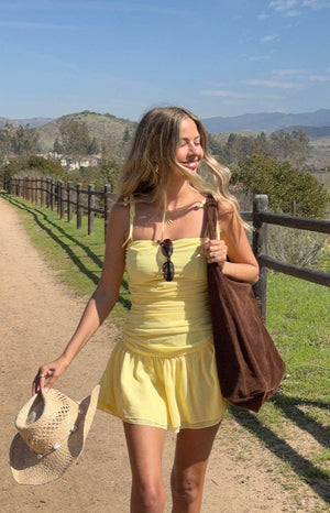 model wearing a yellow chiffon mini dress with ruched and ruffle skirt details