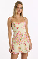 A sweet yellow mini dress with a vibrant pink and orange floral bloom print, featuring a structured bust and dainty tie-shoulder straps, ideal for a garden party or summer event.