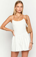 Model wearing a white mini dress with a fit and flare silhouette and shirred material through the bodice, styles with a brown bag and brown boots