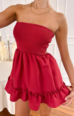 a blonde model poses wearing a red mini dress and gold necklaces