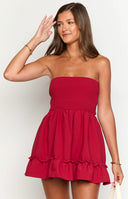 a red mini dress is worn by a blonde model with gold bracelets beside a table with candles