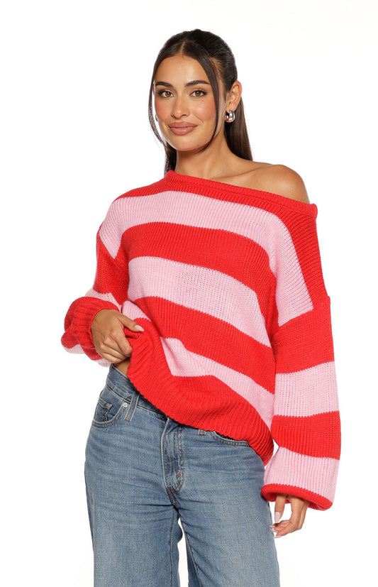 Off-shoulder neckline of a red and pink striped knit sweater with a relaxed fit